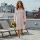 Woman walking on a terrace holding a sunflower wearing a pink gingham sleepshirt with Isla embroidered on the pocket
