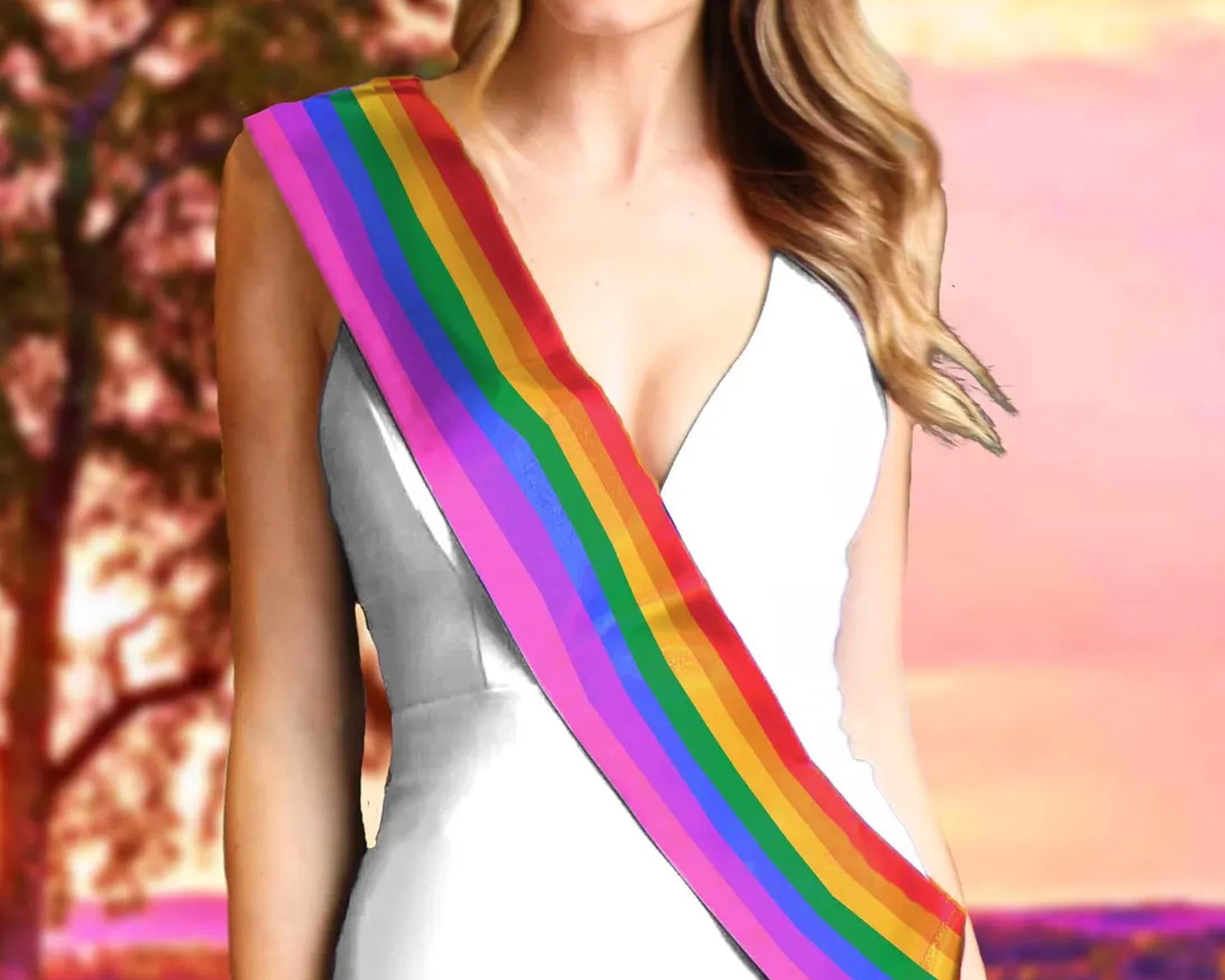  A woman wearing an LGBT-colored sash over a white dress, with a blurred sunset background.