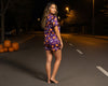 Woman in Halloween-themed outfit standing on a dark street with pumpkins.