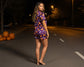 Woman in Halloween-themed outfit standing on a dark street with pumpkins.