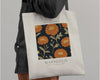 Beige tote bag featuring an October flower design with vibrant orange marigolds on a dark background.