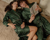 Couple in green satin robes lying on a bed, reading a book.