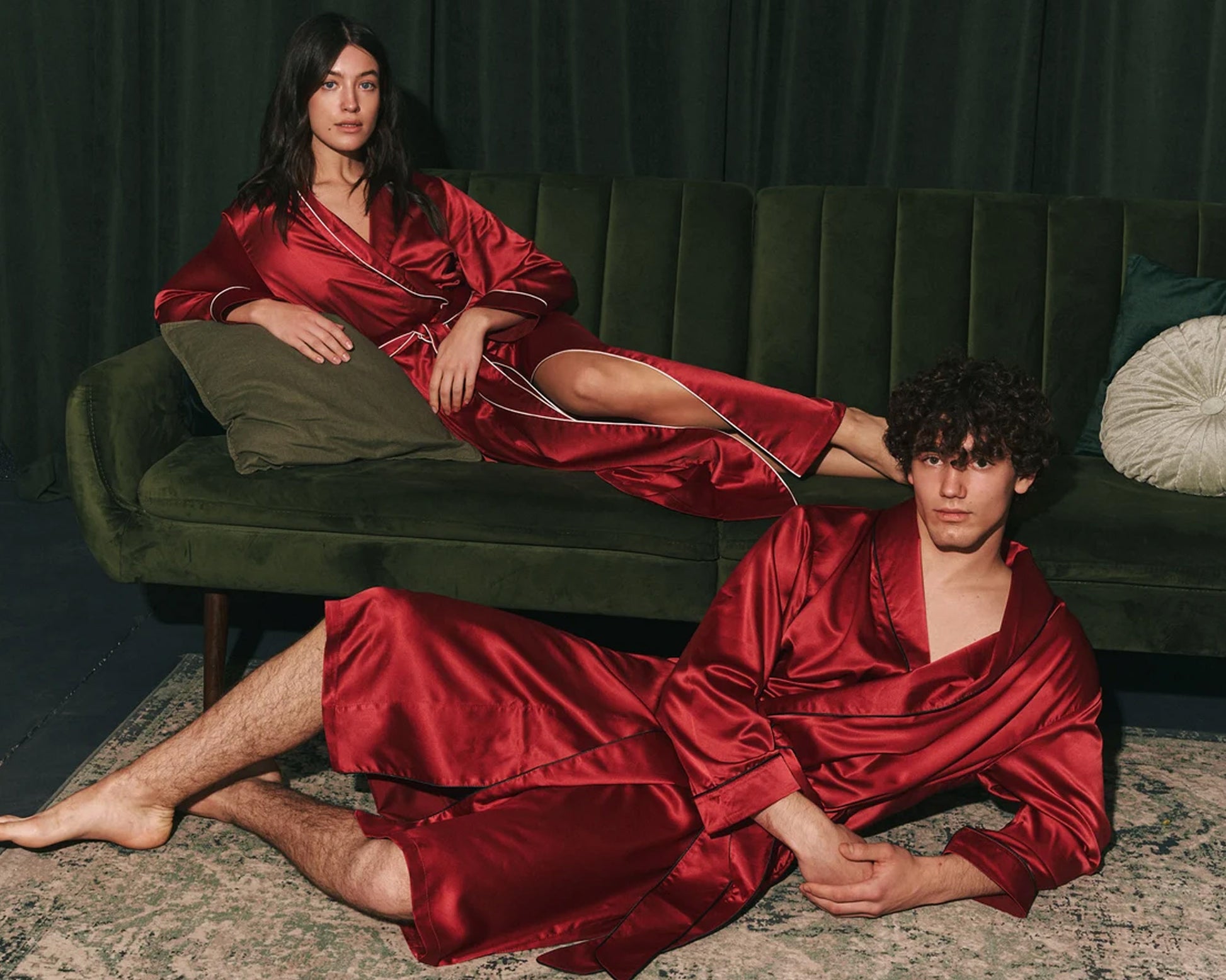 Couple in red satin robes lounging on a green velvet sofa.