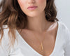 A woman wearing a simple gold bar pendant on a delicate chain.