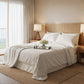 Crisp white satin bed sheets in a bright coastal-style bedroom with a woven cane headboard