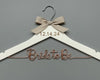 A white wooden hanger with a beige ribbon tied into a bow at the top. The date "12.14.24" is engraved on the hanger, and the phrase "Bride to Be" is crafted in elegant copper wire below.