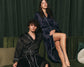  man and woman in satin robes sit on a green velvet couch.