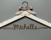 A white wooden hanger with a beige bow tied at the top. The date "12.14.24" is engraved on the hanger, and the name "Michelle" is crafted in copper wire below.