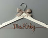  A white wooden hanger with a beige bow tied at the top. The date "3.18.23" is engraved on the hanger, and "Mrs. Kirby" is elegantly crafted in copper wire below.