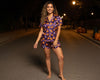 Woman wearing a Halloween-themed purple pajama set on a dark street with pumpkins.