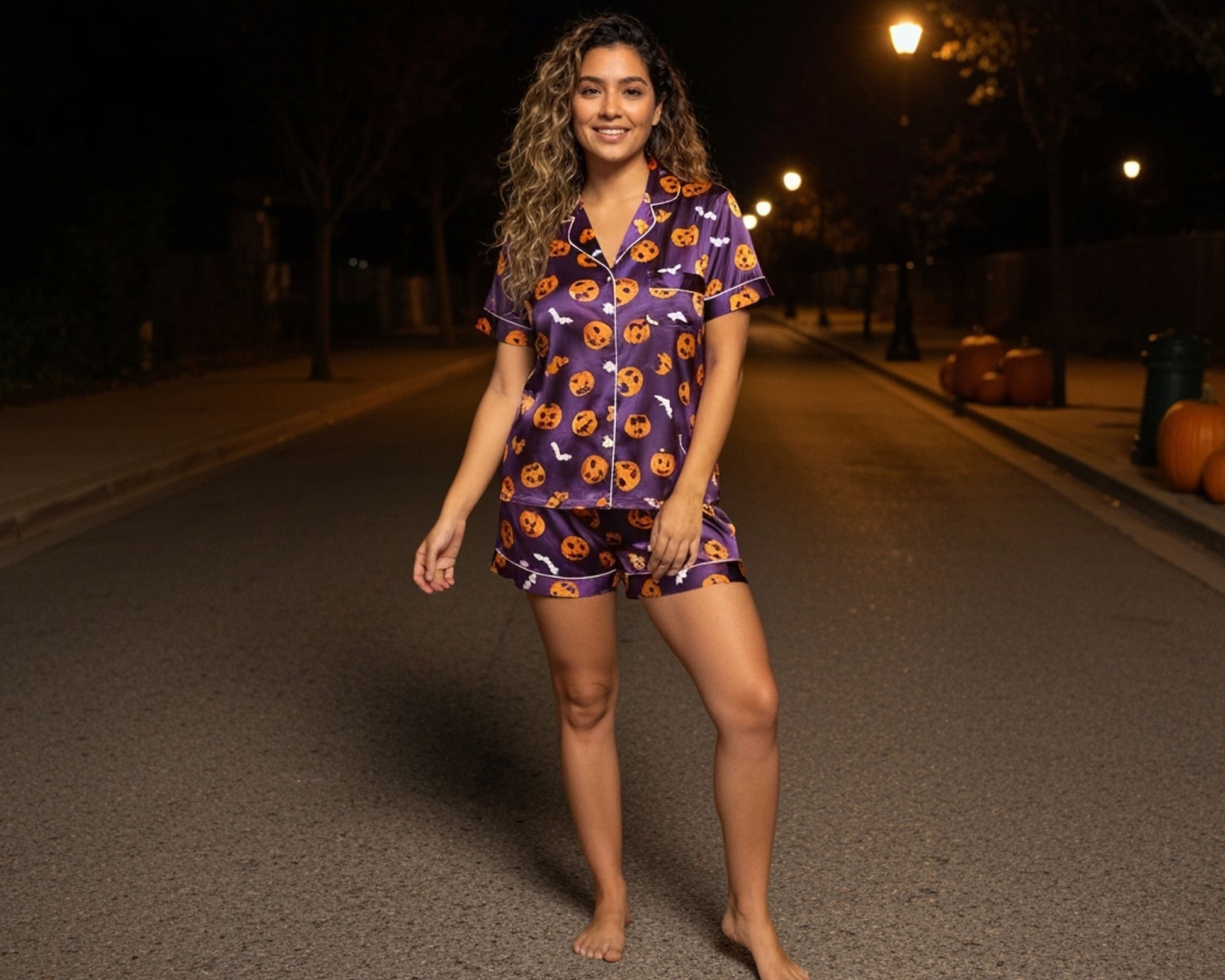 Woman wearing a Halloween-themed purple pajama set on a dark street with pumpkins.