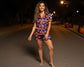 Woman wearing a Halloween-themed purple pajama set on a dark street with pumpkins.