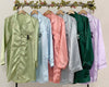 A set of six satin nightshirts in pastel and rich colors hanging on wooden hangers, adorned with embroidered initials.