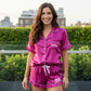 Smiling brunette in magenta satin ruffle shorts set with Nikki and Cheer Leader text