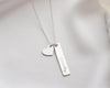  A silver bar pendant necklace engraved with the name "Emiley," accompanied by a heart charm, displayed on soft white fabric.