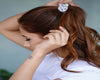 A woman with long, wavy brown hair ties her ponytail with a silver satin scrunchie.
