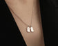 Elegant silver necklace with two engraved name tags, "Emma" and "Jacob," worn over a black outfit.