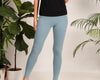 Woman wearing soft blue leggings in a minimalist indoor setting with green plants.