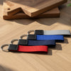Three keychains with red, blue, and black straps on a wooden surface.