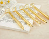 Five gold diamond-topped pens with engraved text placed on an open book, surrounded by white and yellow daisy flowers at blissful world