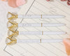 White and gold diamond-topped pens engraved with "Bride Tribe" and a wedding date on lined paper.