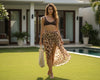 Woman in a leopard print sarong and brown top standing in a garden with a pool in the background