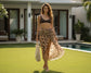 Woman in a leopard print sarong and brown top standing in a garden with a pool in the background