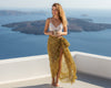 Woman in a leopard print sarong and white top standing on a balcony with a scenic view of the ocean.