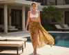 Woman in a white bikini top and tiger print sarong standing by a poolside.