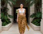 Woman in a white sarong top and tiger striped sarong standing in a tropical setting with plants and stone architecture.