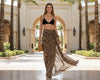 Woman in black bikini top and leopard print skirt walking in a palm tree-lined area.