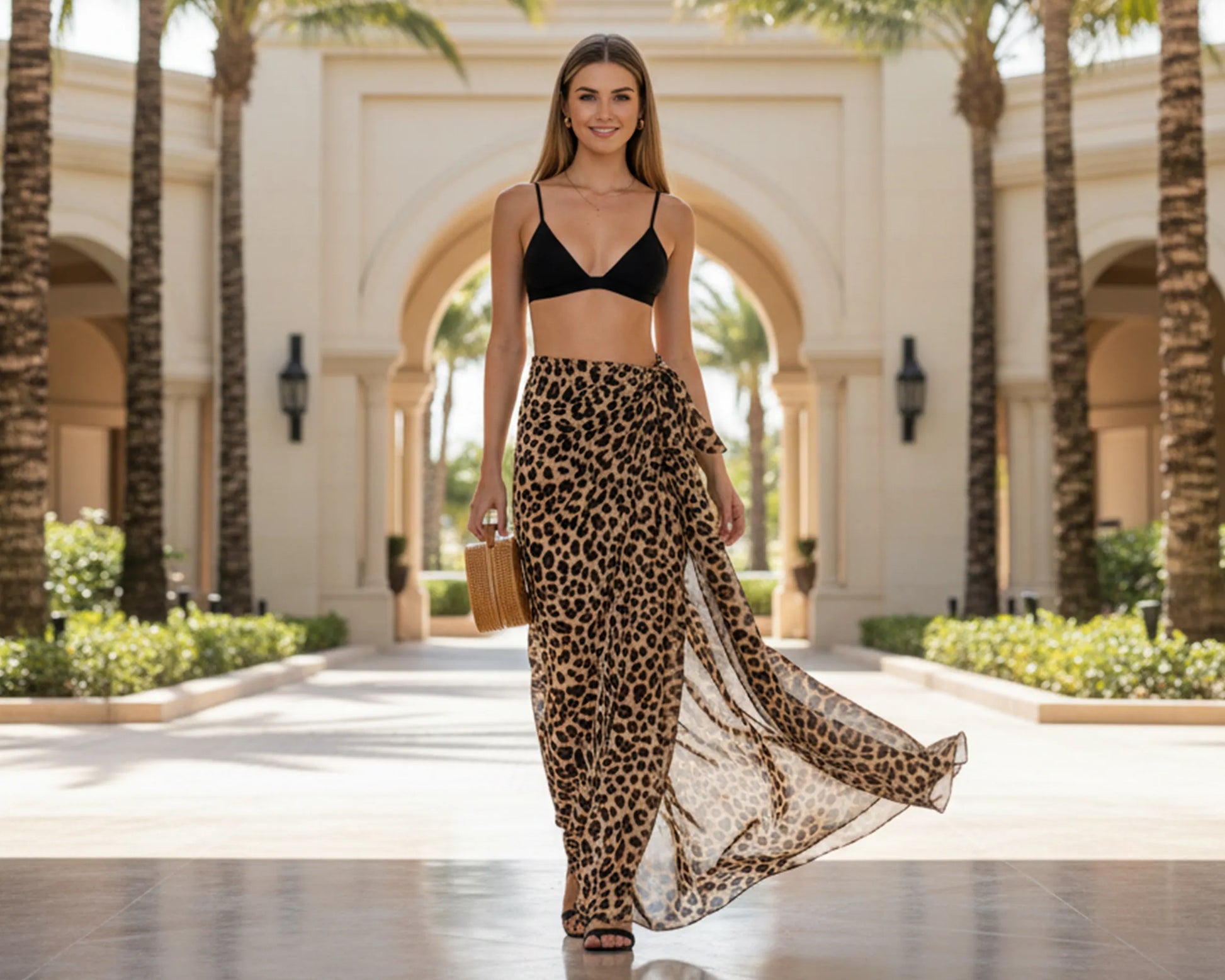 Woman in black bikini top and leopard print skirt walking in a palm tree-lined area.