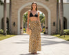 Woman in black bikini top and leopard print skirt standing in front of a building with palm trees.