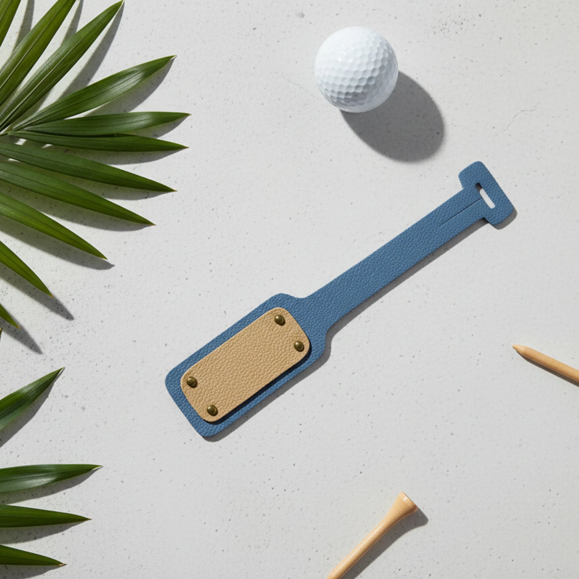 Blue and brown golf club head cover with a golf ball on a light gray surface with green leaves.