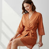 Woman wearing a rust-colored satin robe with lace trim on a white background
