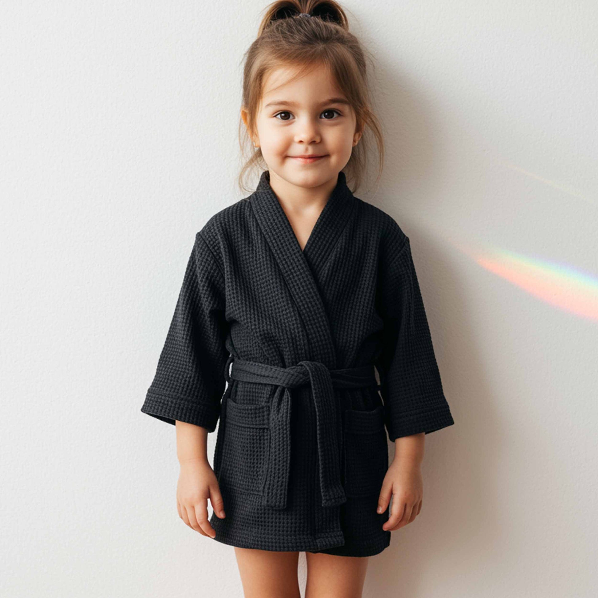 Cute child wearing a black waffle bathrobe, smiling happily