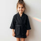 Cute child wearing a black waffle bathrobe, smiling happily