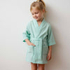 Young girl wearing a light green robe against a plain background
