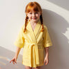 Little girl with braids wearing a yellow waffle robe smiling brightly