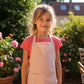 child wearing pink cotton apron in garden setting