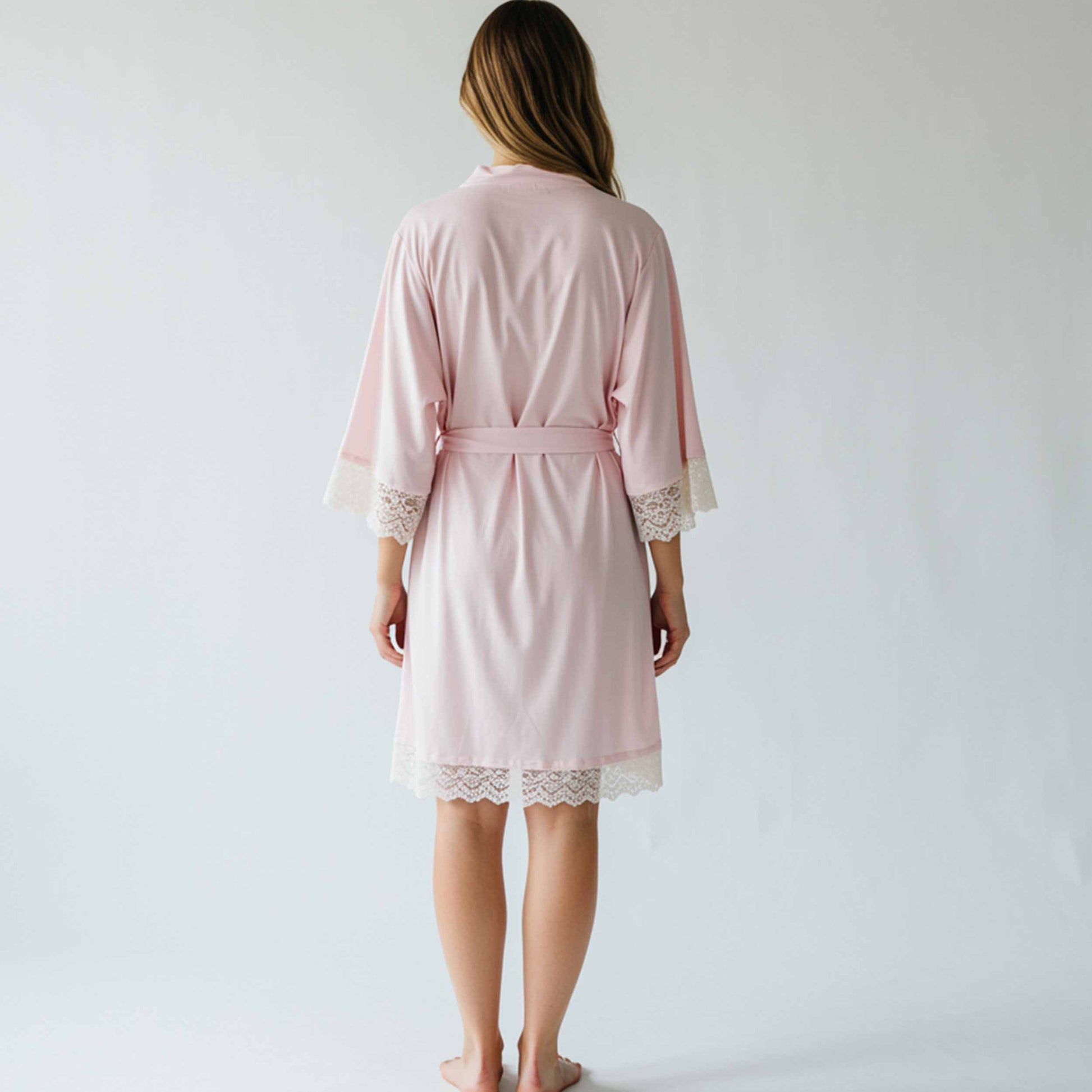 Woman wearing a pink robe with lace trim on a plain background