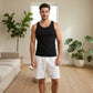 Man wearing a black tank top and white shorts standing in a living room with plants.