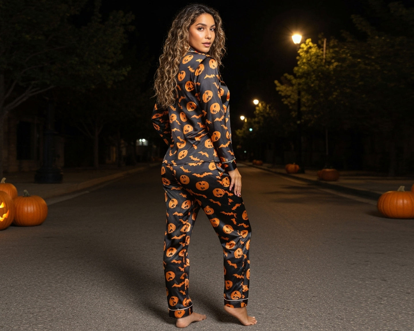 Woman wearing a Halloween-themed onesie with pumpkin pattern in a dark outdoor setting with pumpkins.
