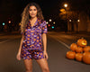 Woman wearing Halloween-themed pajamas with pumpkins and ghosts on a street at night.
