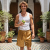 Man in a white tank top and gold shorts holding a drink in a courtyard with plants.