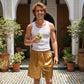 Man in a white tank top and gold shorts holding a drink in a courtyard with plants.